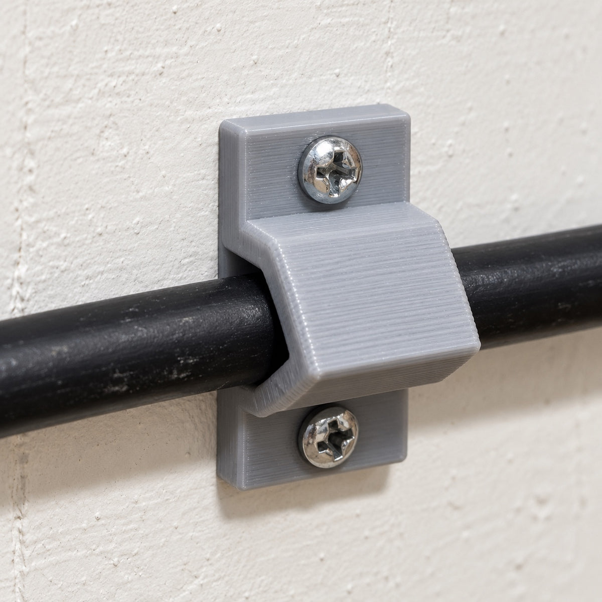 Grey screw-down cable saddle installed over a black extension cord